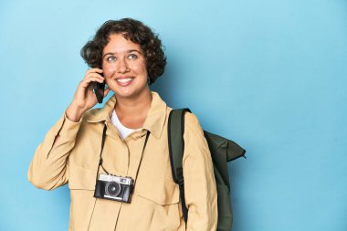 Klasik kameralı, sırt çantalı, telefonla konuşan mutlu genç gezgin kadın..