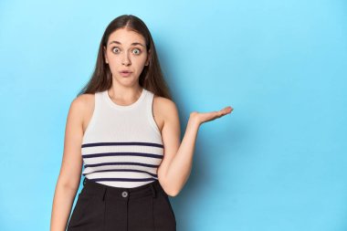 Çizgili bluzlu bir kadın mavi bir stüdyo arkaplanında poz veriyor..