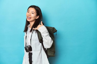 Genç Asyalı gezgin, parmaklarıyla bir cep telefonu hareketi göstererek maceraları yakalamaya hazır..