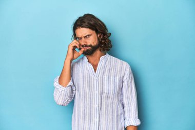 Mavi çizgili gömlekli sakallı bir adam, dudakları dudaklarında mavi bir stüdyo..