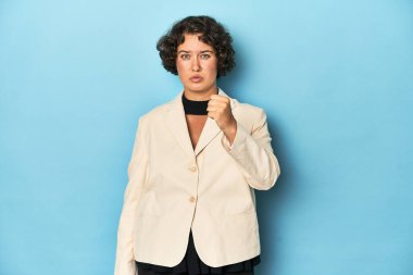 Zarif beyaz ceketli genç bir kadın kameraya yumruğunu gösteriyor, agresif bir yüz ifadesi..