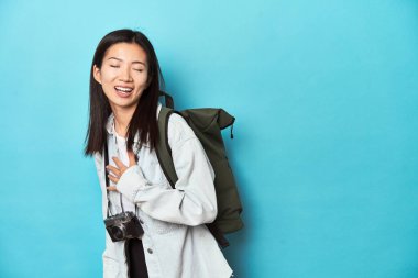 Genç Asyalı gezgin maceraları yakalamaya hazır elini göğsüne koyup yüksek sesle kahkaha atıyor..