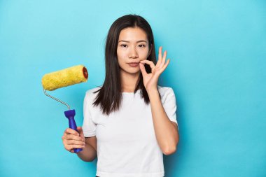 Boyalı silindirli genç bir Asyalı kadın, DIY konsepti, parmakları dudaklarında bir sır saklayan.