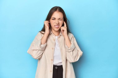 Mavi arka planda, mavi gömlekli, elleri kulaklı şık genç bir kadın..
