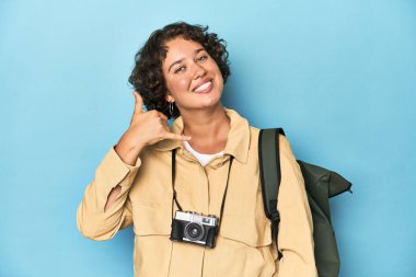 Klasik kameralı genç gezgin kadın parmaklarıyla bir cep telefonu hareketi gösteriyor..