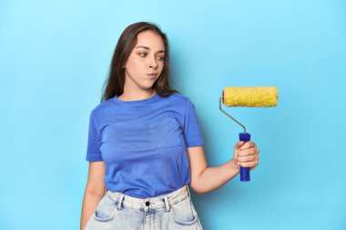 Mavi stüdyoda sarı boya silindirli beyaz bir kadın..