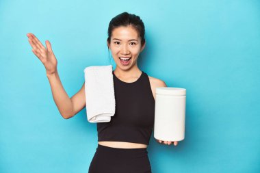 Protein şişesi ve spor salonu düzeniyle genç Asyalı sporcu, hoş bir sürpriz alıyor, heyecanlı ve el kaldırıyor..