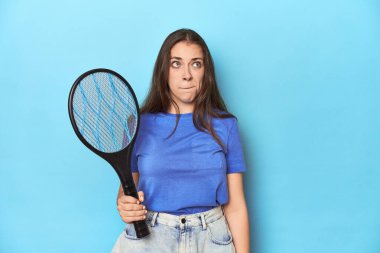 Mavi arka planda elektrikli böcek bayıltıcısı olan kadın kafası karışmış, kuşkulu ve kendinden emin değil..