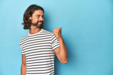 Çizgili gömlekli sakallı adam, mavi arka plan noktaları başparmak uzakta, gülüyor ve kaygısız..