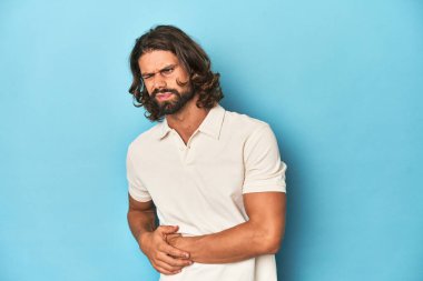Beyaz polo giyen uzun saçlı bir adam, mavi stüdyo, karaciğer ağrısı, mide ağrısı var..
