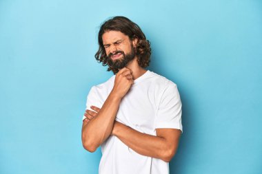 Beyaz gömlekli sakallı bir adam, mavi arka planda virüs ya da enfeksiyon yüzünden boğaz ağrısı var..