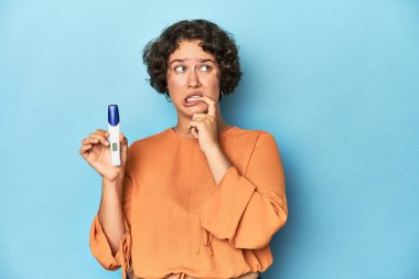 Hamilelik testi tutan genç bir kadın, stüdyo geçmişi rahat bir şekilde fotokopi odasına bakan bir şey düşünüyor..