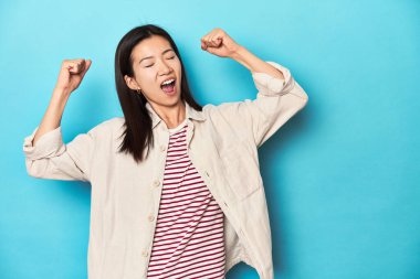 Katmanlı tişörtlü, çizgili tişörtlü Asyalı bir kadın zaferden sonra yumruğunu kaldırıyor..