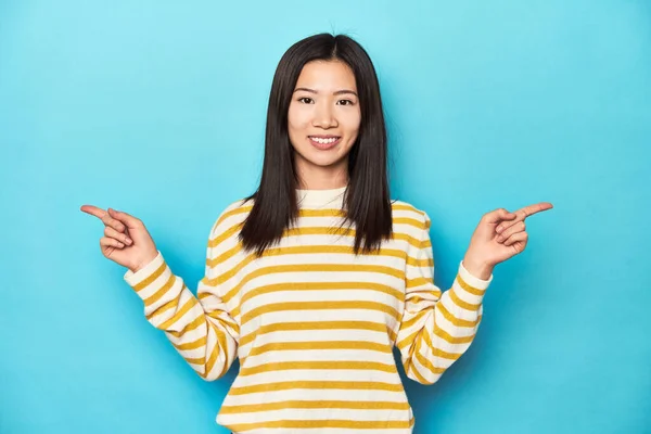 穿着条纹黄色毛衣的亚洲女人 指着不同的复制空间 选了一件 用手指显示出来 — 图库照片
