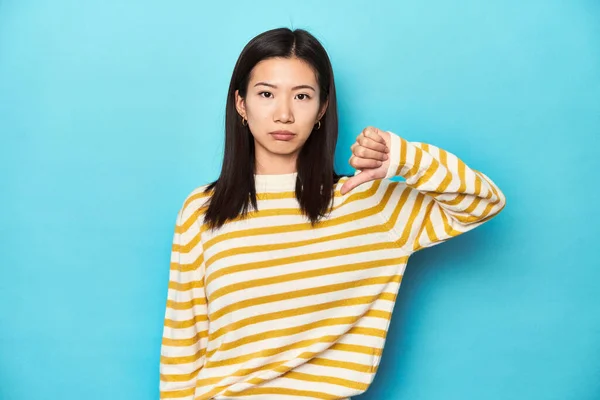 身穿条纹黄色毛衣的亚洲女人表现出不喜欢的姿态 低垂了大拇指 不同意的概念 — 图库照片