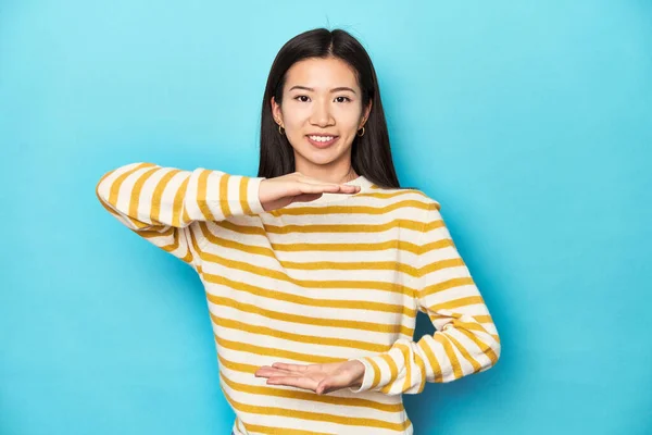 穿着条纹黄色毛衣的亚洲女人 双手拿着一样东西 做产品演示 — 图库照片