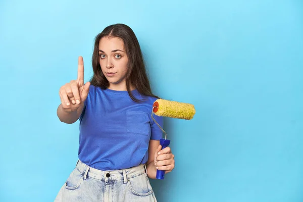 Jonge Vrouw Met Gele Verfrol Een Blauwe Achtergrond Met Nummer — Stockfoto