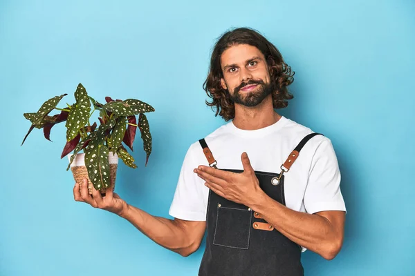 青いスタジオに植物を抱えているひげを持つ長髪の庭師 — ストック写真