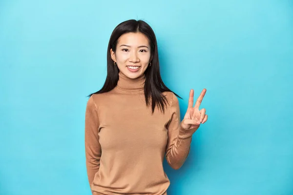 身穿棕色高领毛衣的年轻亚洲女子 展示出胜利的迹象 面带微笑 — 图库照片