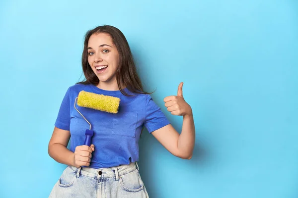 Young Woman Yellow Paint Roller Blue Background Smiling Raising Thumb — Stock Photo, Image