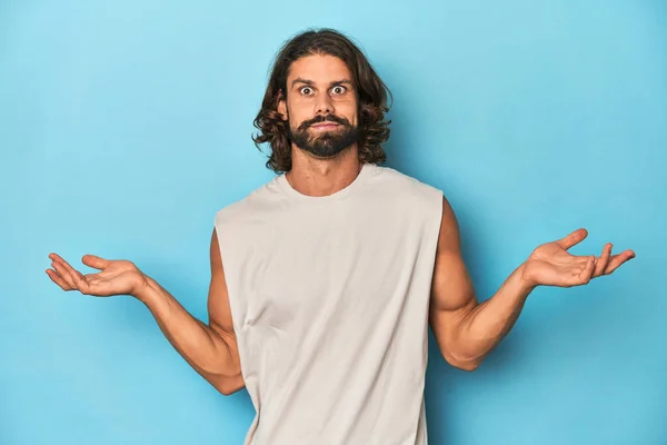 Bearded Man Tank Top Blue Backdrop Doubting Shrugging Shoulders Questioning — Stock Photo, Image