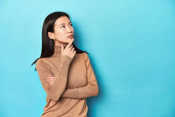穿着棕色毛衣的年轻亚洲女人 带着怀疑和怀疑的表情侧视着四周 — 图库照片