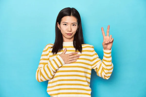 身穿条纹黄色毛衣的亚洲妇女宣誓 双手放在胸前 — 图库照片