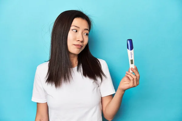 Young Asian woman holding a pregnancy test, studio shot.