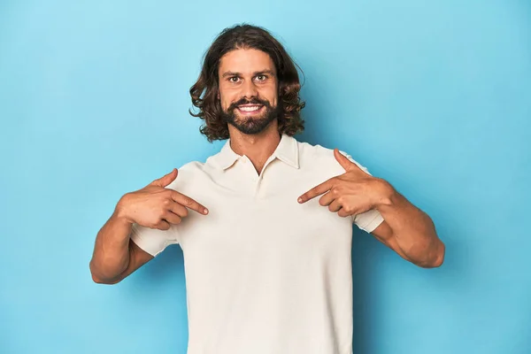 Long Haired Man White Polo Blue Studio Surprised Pointing Finger — Stock Photo, Image