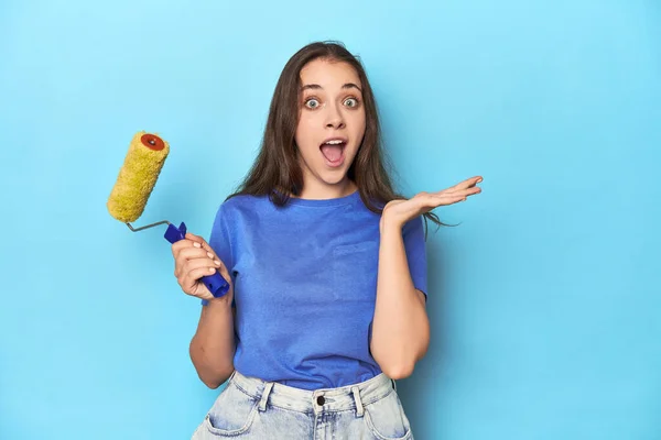 Jovem Mulher Com Rolo Tinta Amarela Fundo Azul Surpreso Chocado — Fotografia de Stock