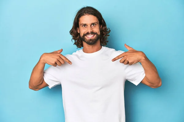 Bearded Man White Shirt Blue Backdrop Surprised Pointing Finger Smiling — Stock Photo, Image