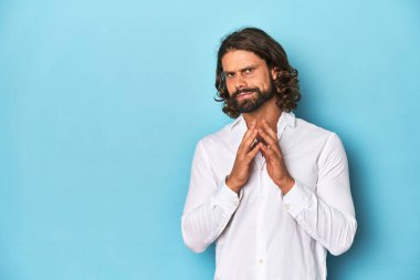 Beyaz gömlekli sakallı bir adam, mavi arka planlı, bir plan hazırlıyor..