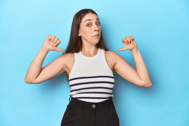 Çizgili bluzlu bir kadın mavi bir stüdyoda poz veriyor gururlu ve kendinden emin, örnek olarak..