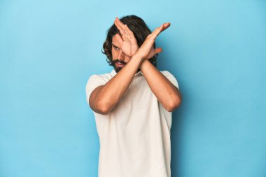 Beyaz polo salonundaki uzun saçlı adam, iki kolu çapraz tutuyor, inkar kavramı..