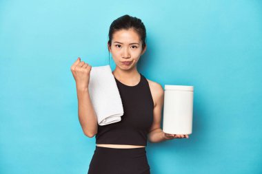 Protein şişesi olan genç Asyalı sporcu, spor salonu düzeneği, kameraya yumruk atma, agresif yüz ifadesi..