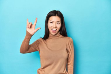 Kahverengi balıkçı yakalı genç Asyalı kadın boynuzlarını devrim konsepti olarak gösteriyor..