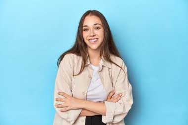 Mavi arka planda tişörtlü şık genç bir kadın gülüyor ve eğleniyor..