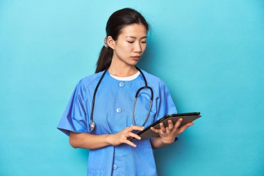 Tabletli Asyalı hemşire. Stüdyoda çekilen bir görüntüyü inceliyor..