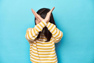 Çizgili sarı kazaklı Asyalı kadın, iki kolu çapraz tutuyor, inkar kavramı.