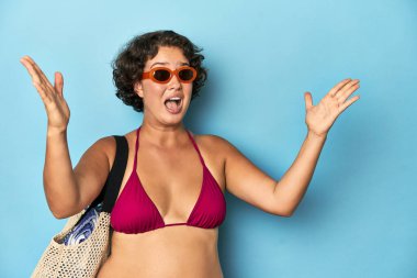 Bikinili genç bir kadın kumsal çantası ile hoş bir sürpriz alıyor, heyecanlı ve el kaldırıyor..