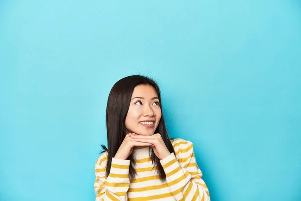 Asian Woman Striped Yellow Sweater Keeps Hands Chin Looking Happily — Stock Photo, Image
