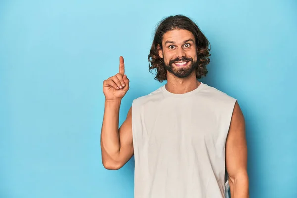 Bearded Man Tank Top Blue Backdrop Showing Number One Finger — Stock Photo, Image