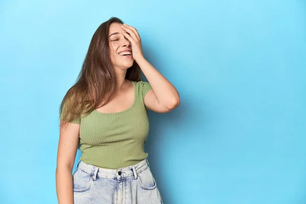 Jonge Blanke Vrouw Een Groene Top Een Blauwe Achtergrond Lachen — Stockfoto
