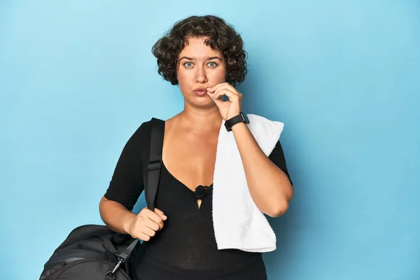 Young sportswoman with gym backpack and towel with fingers on lips keeping a secret.