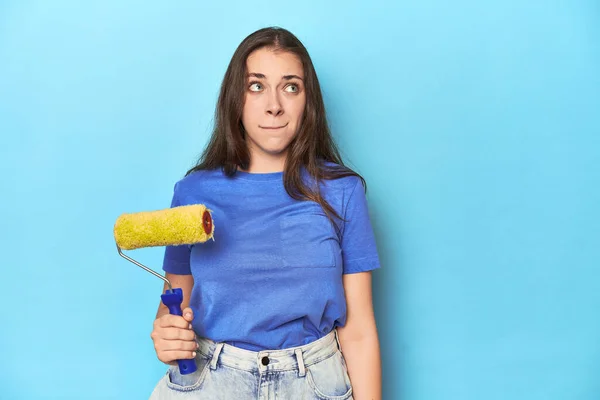 Young Woman Yellow Paint Roller Blue Background Confused Feels Doubtful — Stock Photo, Image