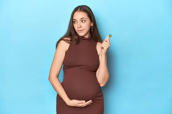 青いスタジオで赤ん坊を抱えている女性を期待 — ストック写真