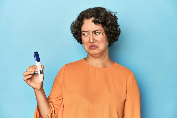 Young Caucasian woman holding a pregnancy test, studio blue background.