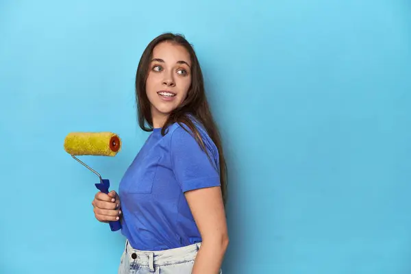 Young Woman Yellow Paint Roller Blue Background Looks Aside Smiling — Stock Photo, Image