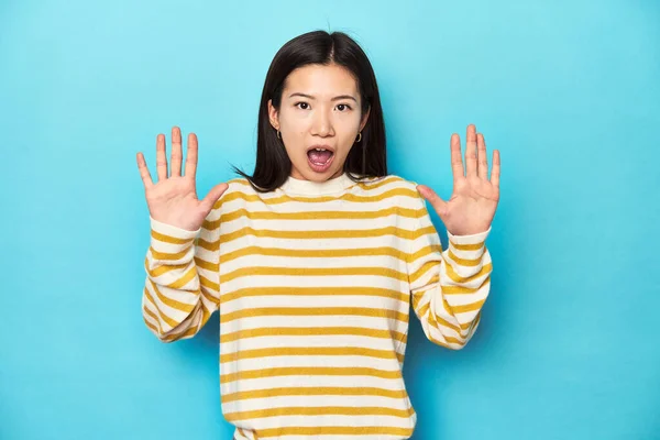 穿着条纹黄色毛衣的亚洲女人 得到了一个愉快的惊喜 兴奋地举起双手 — 图库照片