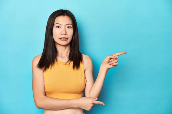 穿着夏黄上衣的亚洲女人 演播室的布置 用食指指向一个复制的空间 震惊极了 — 图库照片